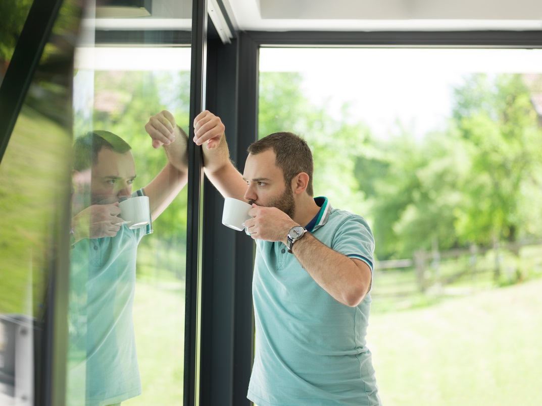 Man drinking morning coffee by the window in his home.