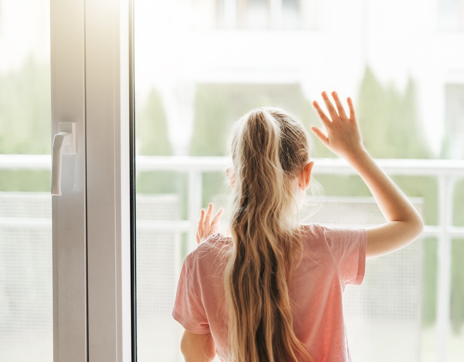 A little girl looking through a window at home.